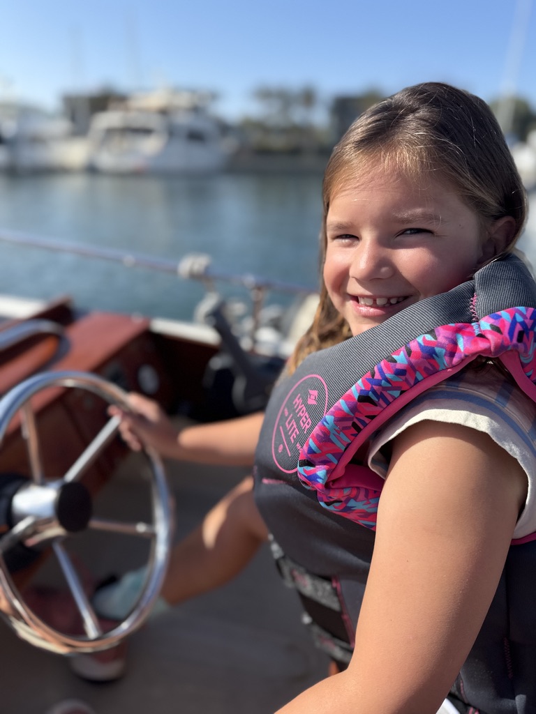 A young sailor smiling at the helm in the marina